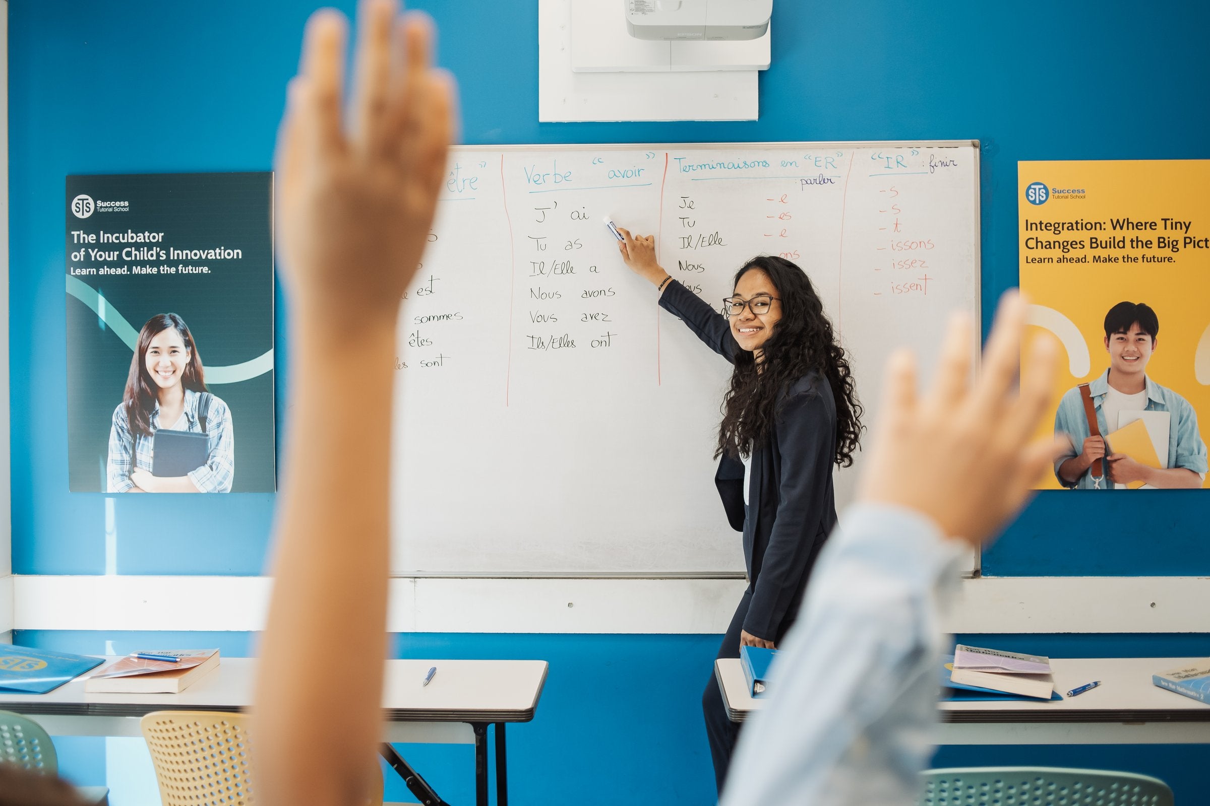 An STS teacher teaching French verbs while students raise their hands